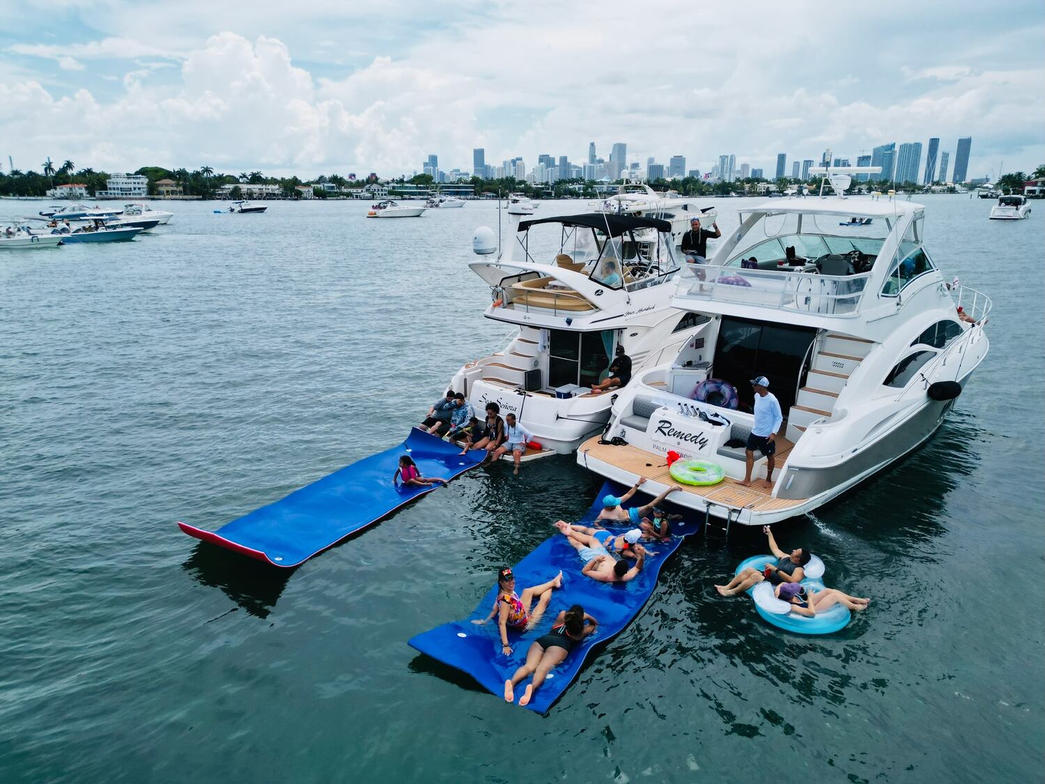 Two yachts rafted up in Biscayne Bay with guests floating on water mats