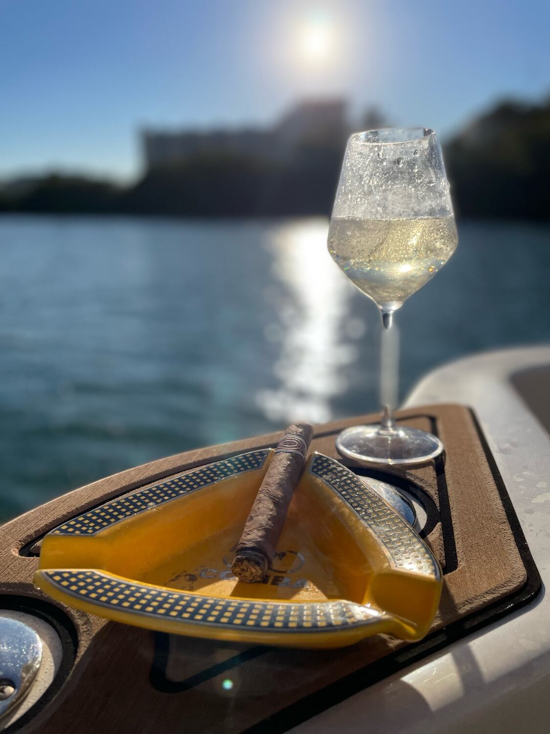 A glass of white wine on the gunwale with the sun on the water